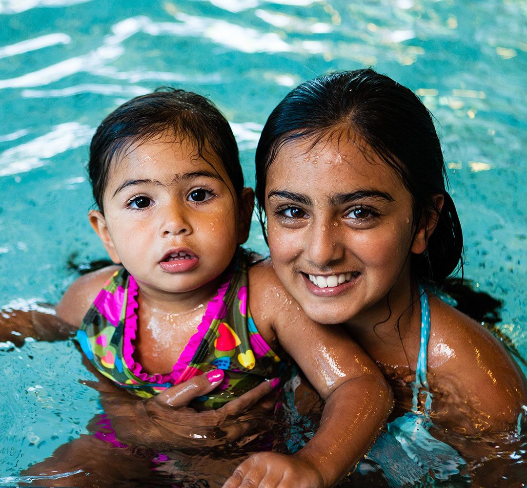 pool schedules smiling young woman holds cute girl in the water