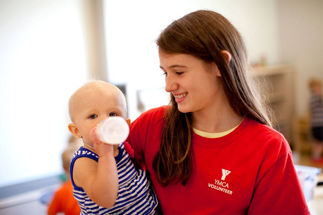 Babysitting Course Youth in YMCA volunteer shirt holds baby