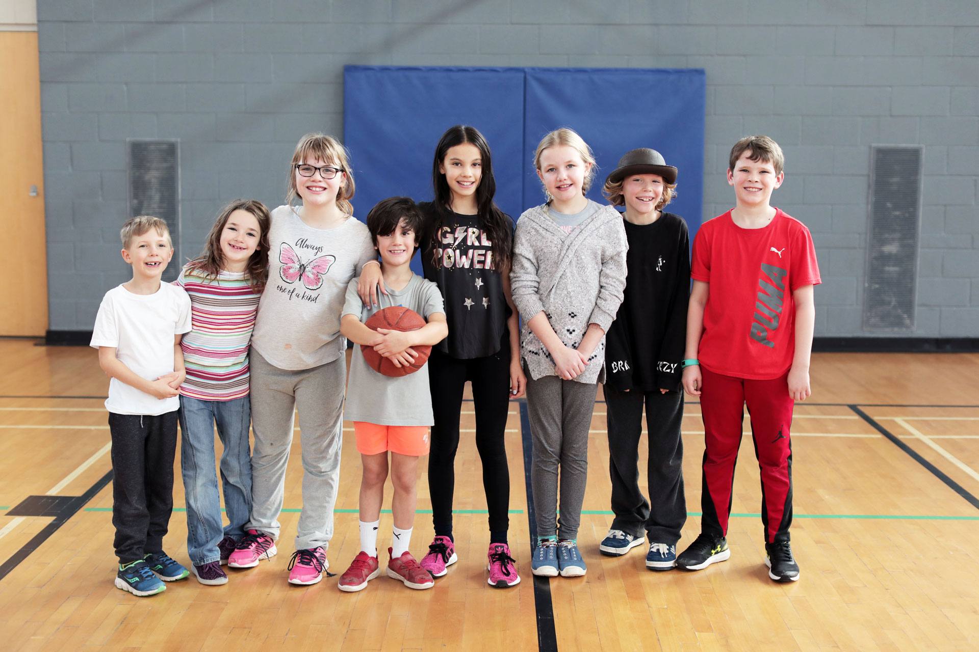 8 smiling kids of different ages standing in gymnasium together