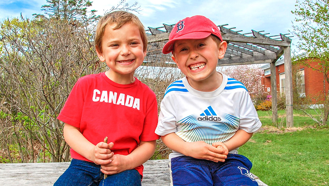 Summer Camp (grid content) Two boys sitting on a bench outside smiling