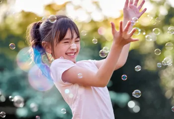 happy girl playing with bubbles outside in the sunshine