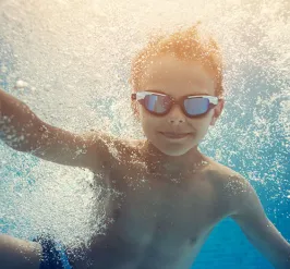 boy wearing goggles underwater surrounded by bubbles after jumping into pool