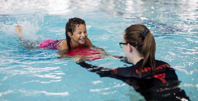 instructor teaching child to swim with kickboard