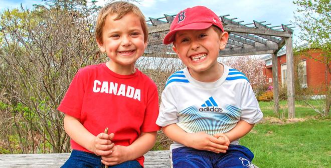 Two boys sitting on a bench outside smiling