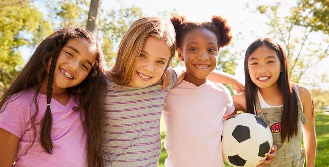 four happy girls outside with soccer ball