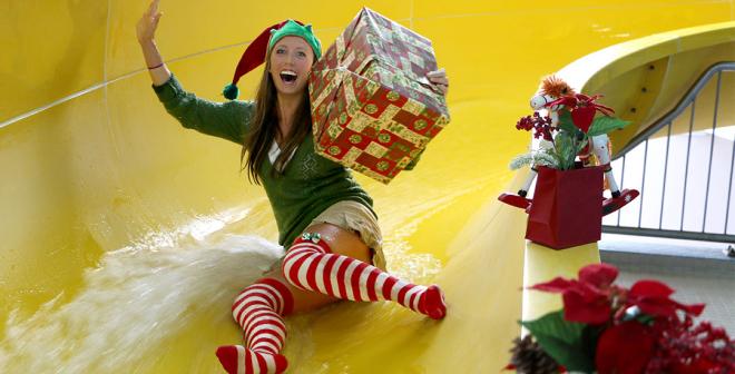 excited elf holds a present as she slides down yellow water slide at H2O