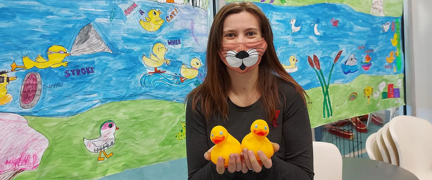 staff member holding rubber ducks in front of hand-drawn banner
