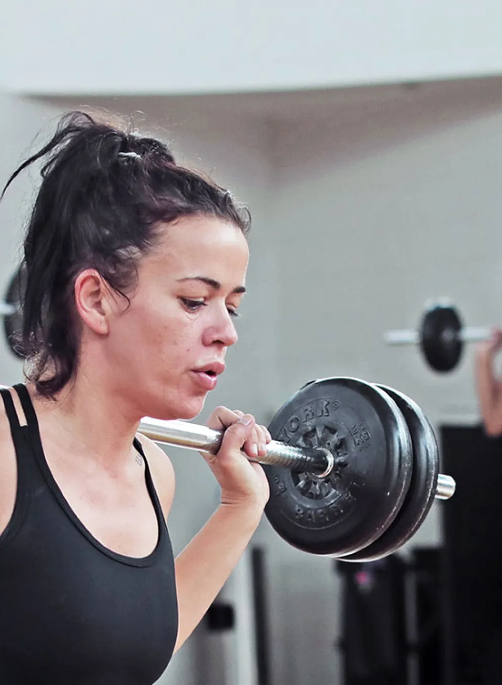 young woman performs a barbell lunge in a group fitness class
