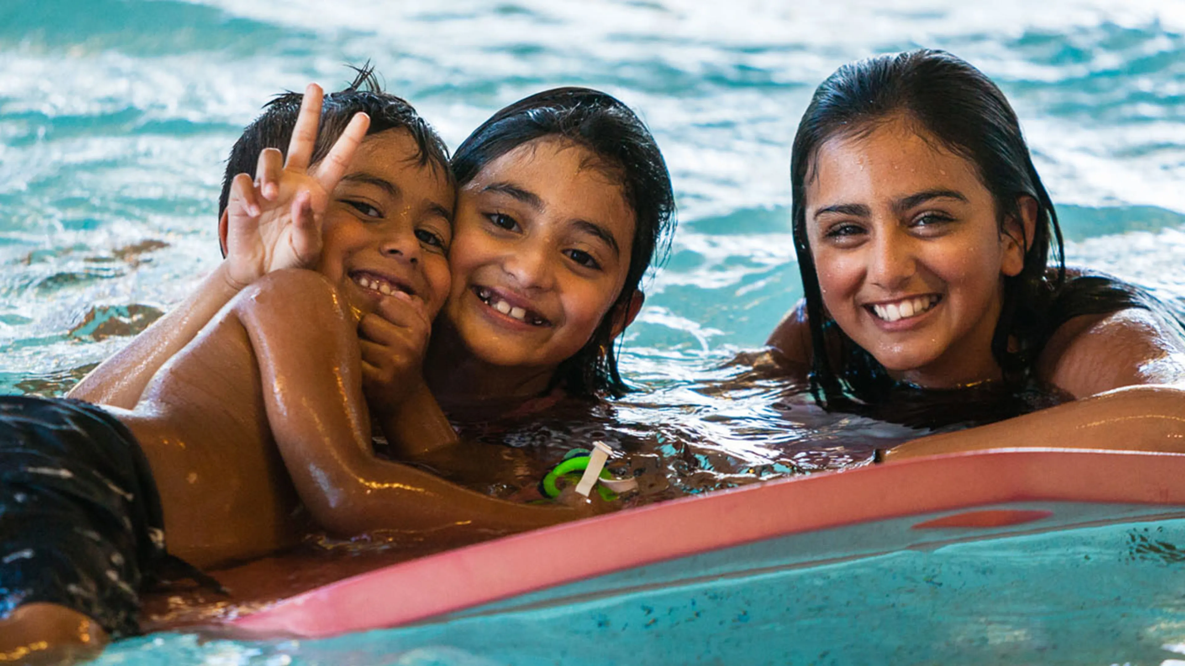 Three kids smiling in the pool