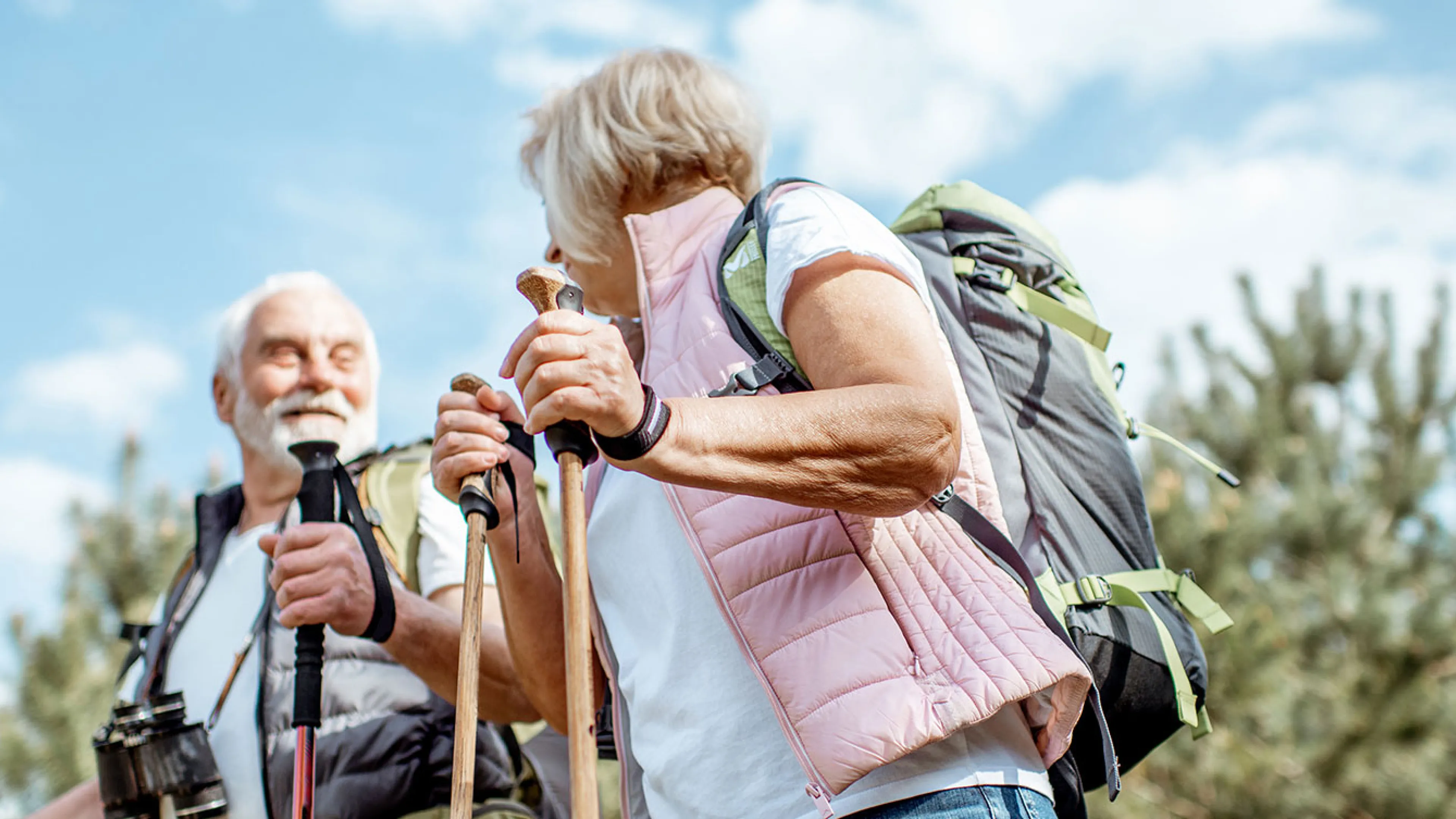 senior couple with backpacks and trekking poles enjoying nature on a sunny day