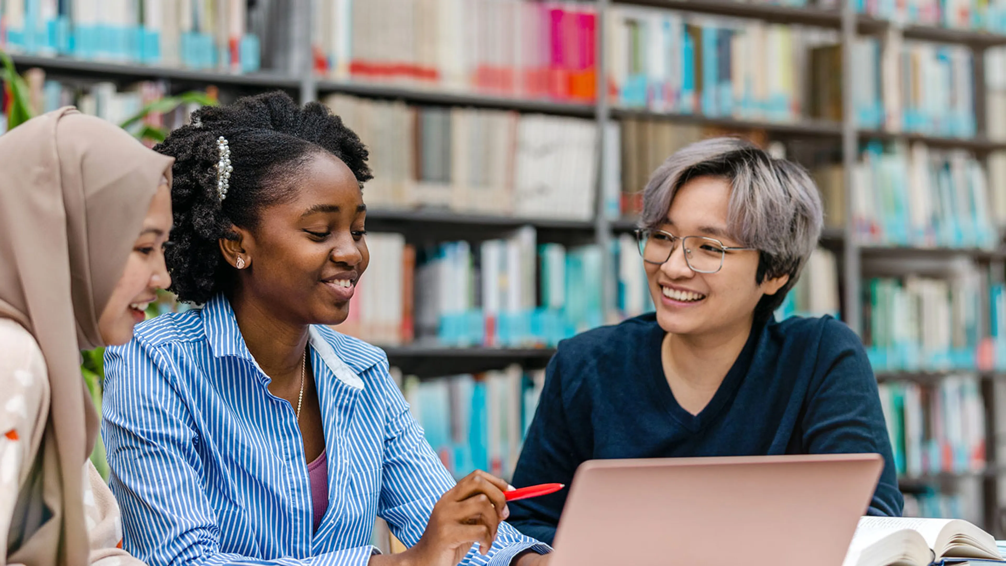 three young people gather at a table with a laptop and notebooks