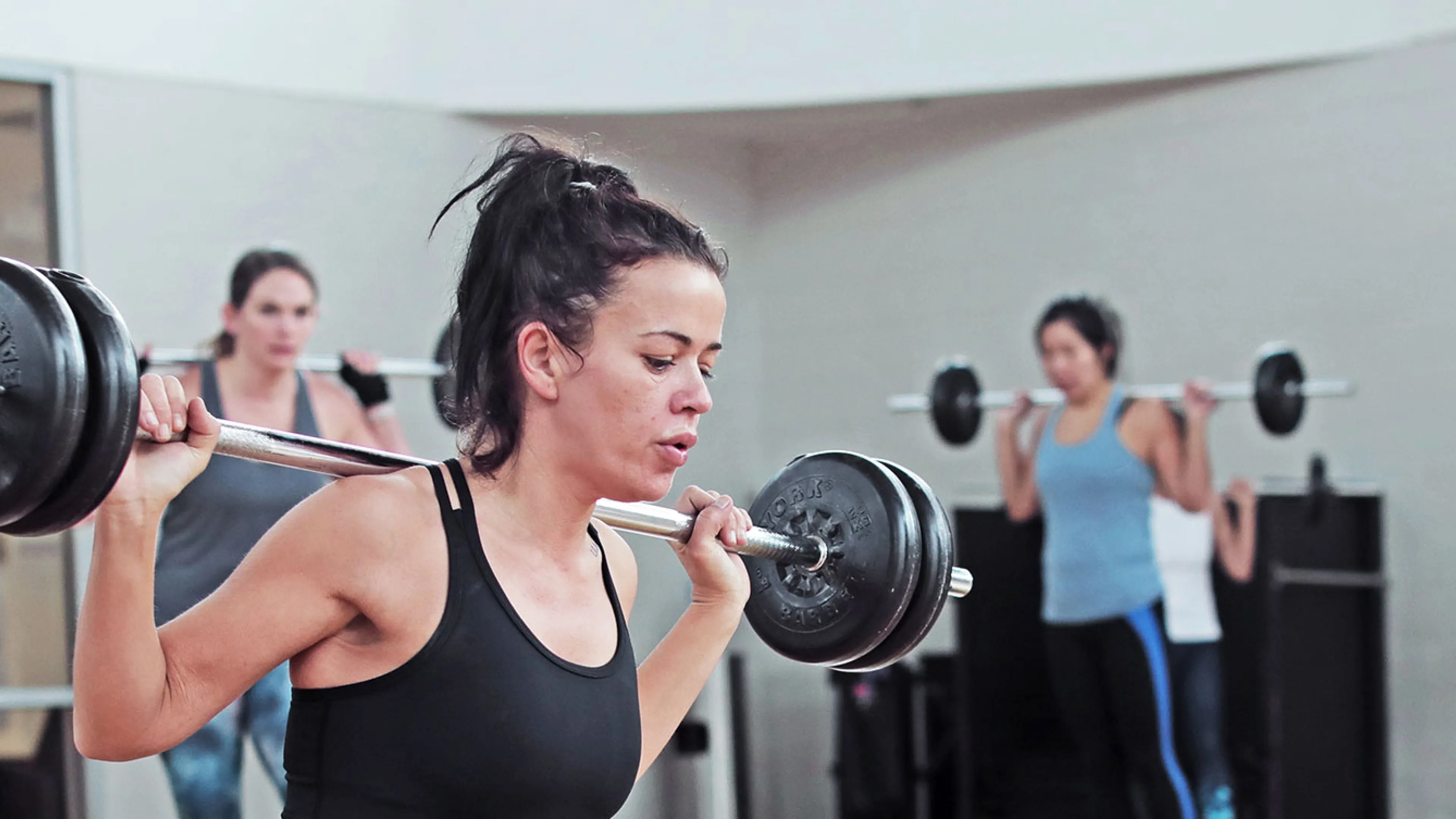 young woman performs a barbell lunge in a group fitness class