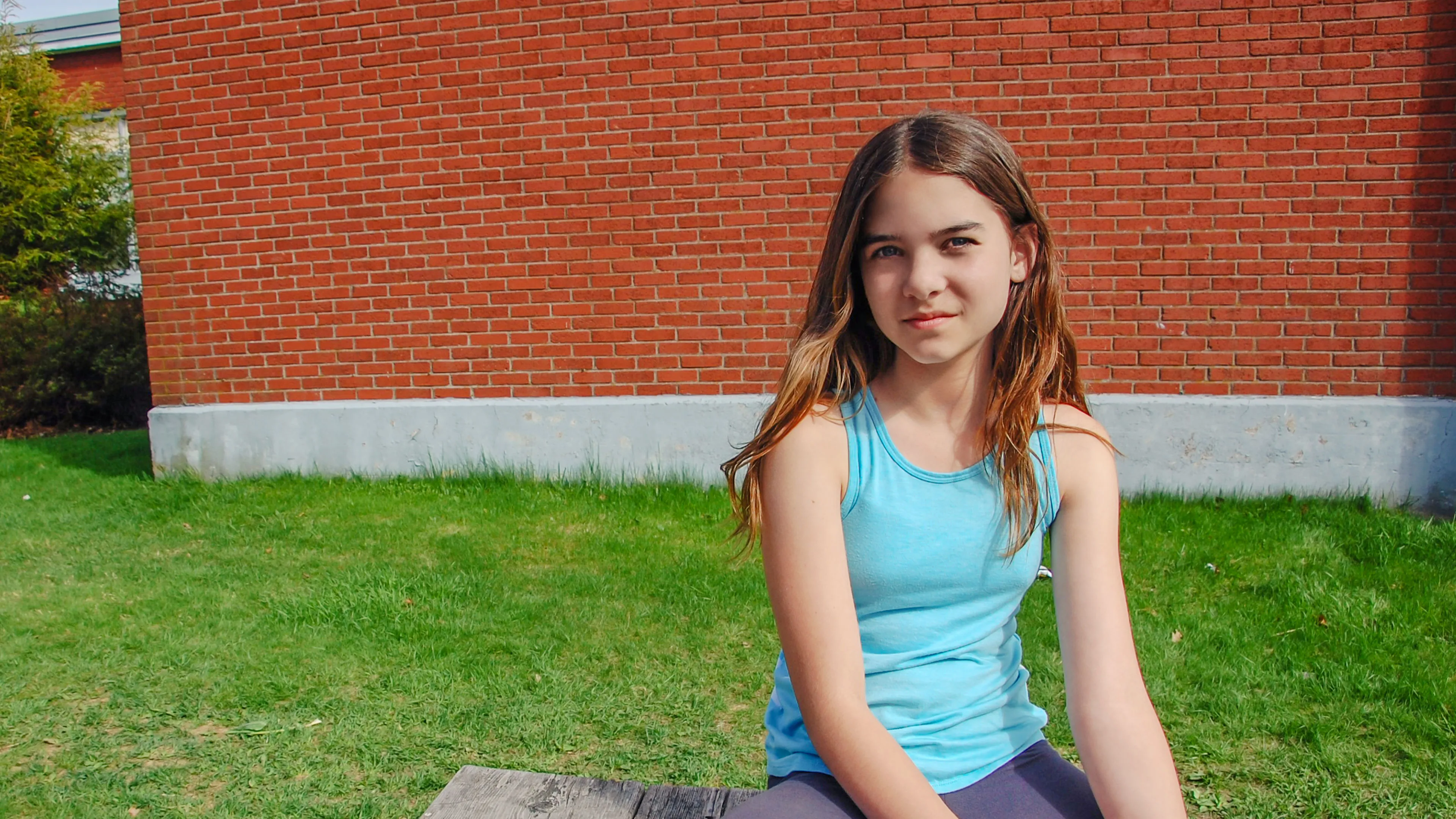 school-aged youth sitting in front of brick building
