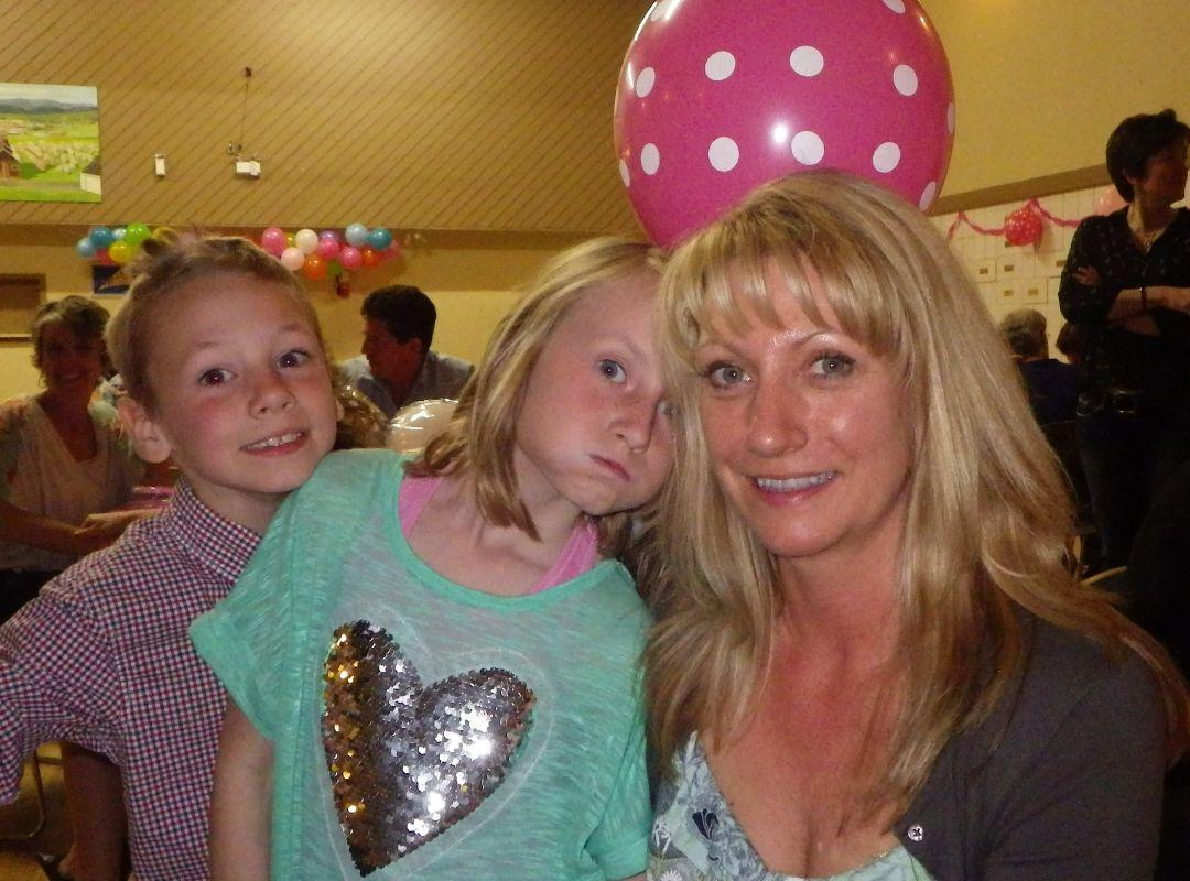 Allyson Graf and her two young children at a party in a gym with balloons in the background. 