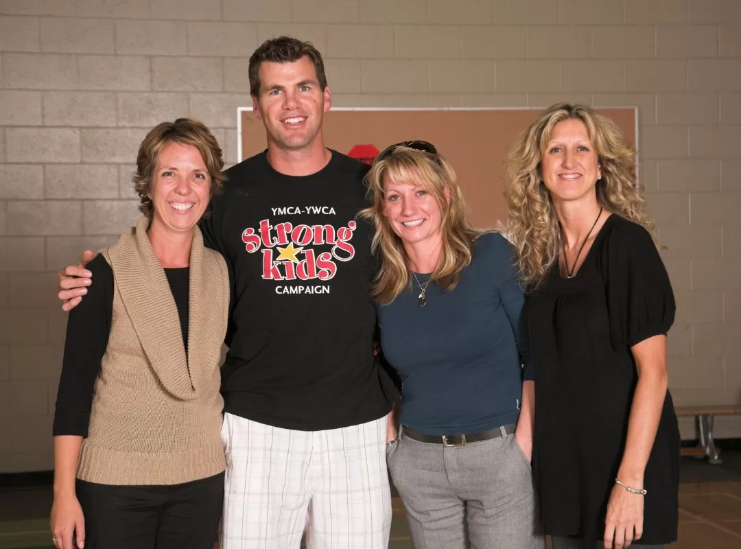 Four adults standing with their arms around each other in a gym. 