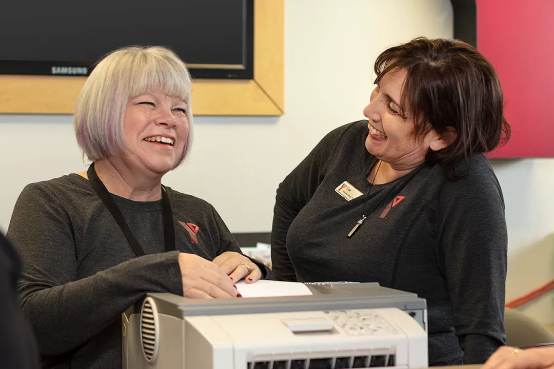 Monica and Sue laughing by a printer