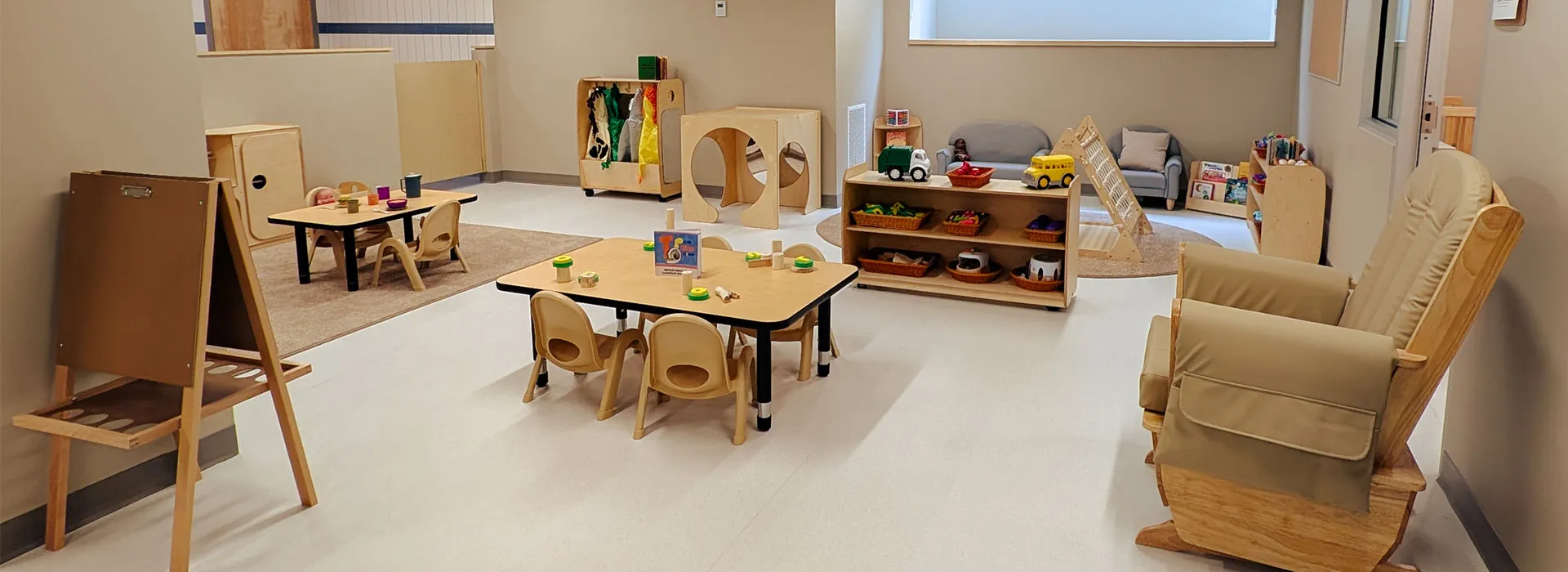 child care room with tables, toys, books, and comfy chairs