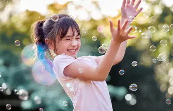 happy girl playing with bubbles outside in the sunshine