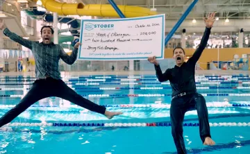 2 men jumping in a pool with a huge cheque
