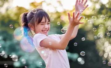 happy girl playing with bubbles outside in the sunshine