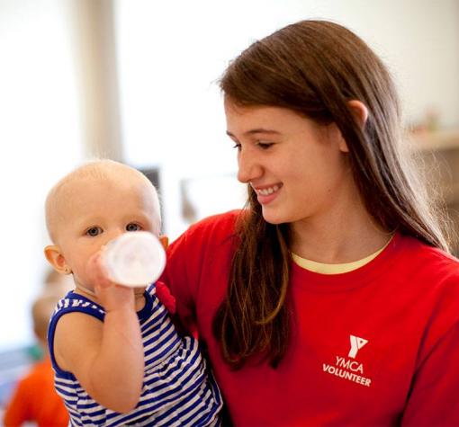 Babysitting Course Youth in YMCA volunteer shirt holds baby