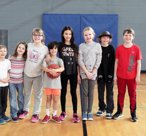 8 smiling kids of different ages standing in gymnasium together