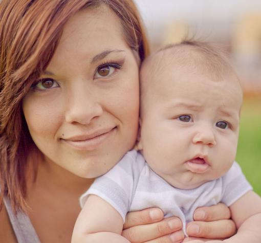YPP Teaser A close up photo of a young mother with brown eyes and dark red hair holding a three month old baby in a white shirt.
