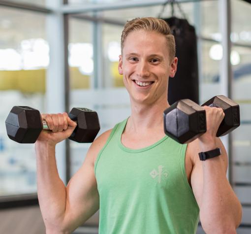 young man lifting dumbbells smiling at camera