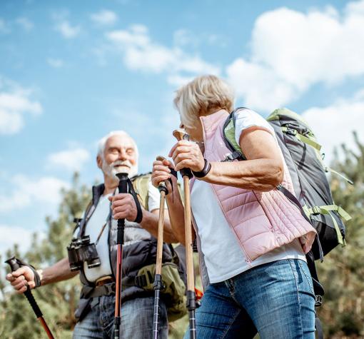 senior couple with backpacks and trekking poles enjoying nature on a sunny day