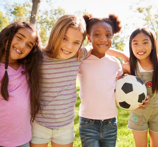 four happy girls outside with soccer ball